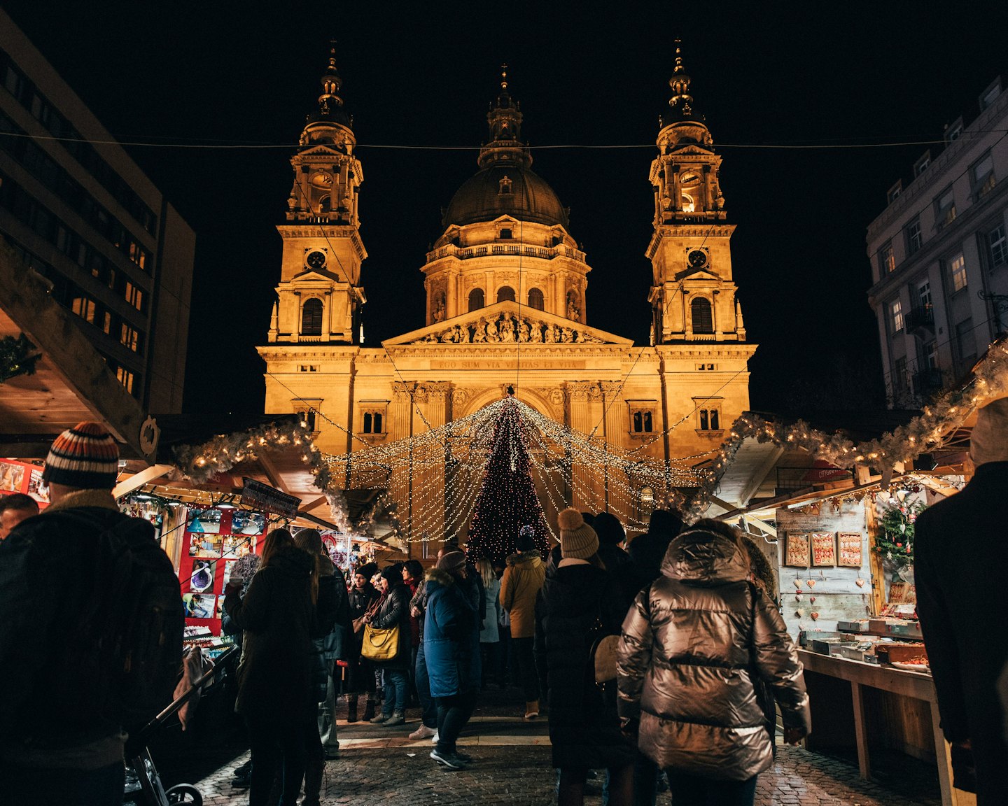 Persone che curiosano tra bancarelle di legno illuminate in un vivace mercato di Natale.