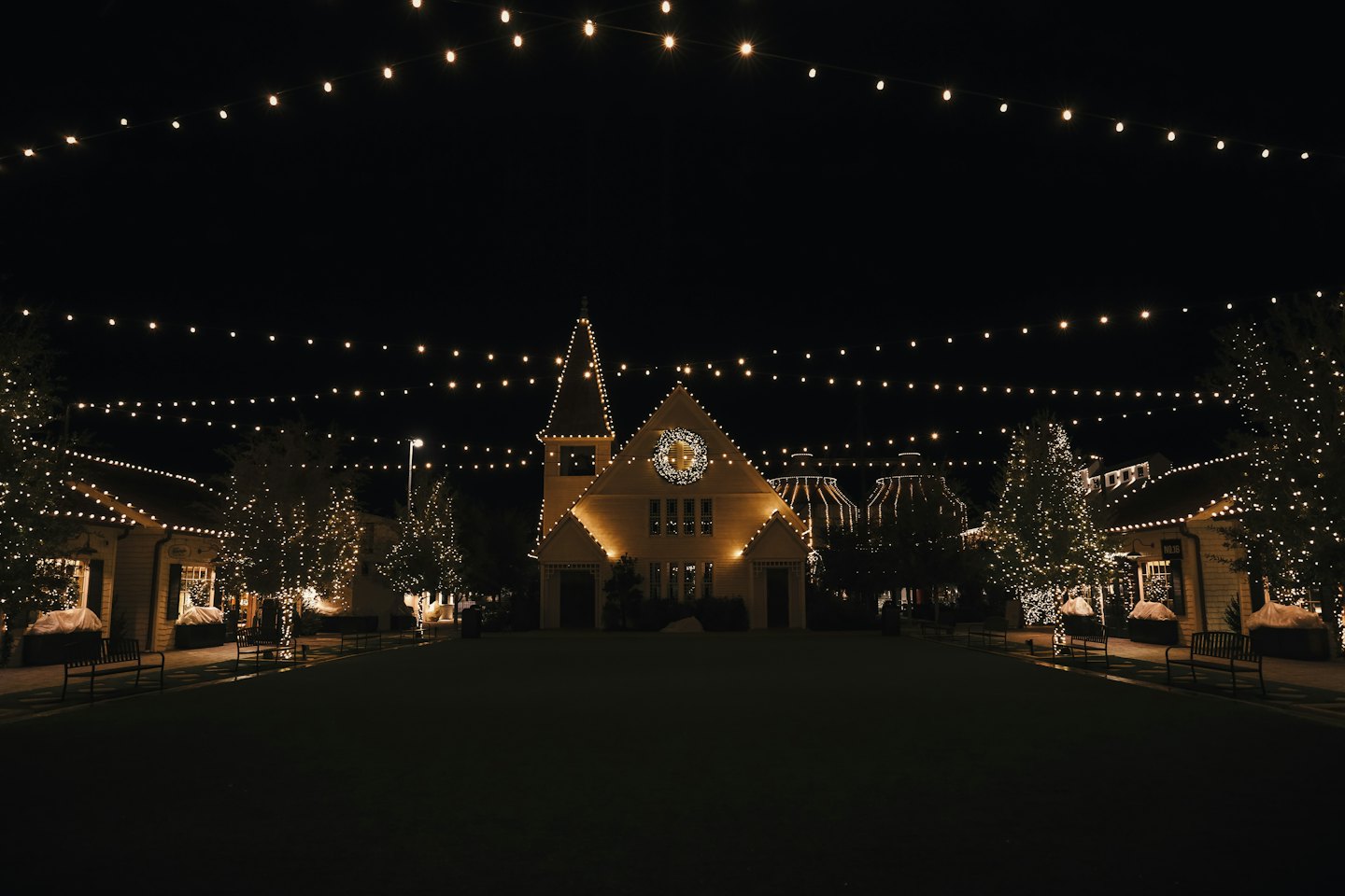 Piazza di paese festosa illuminata da fili di luci dorate.